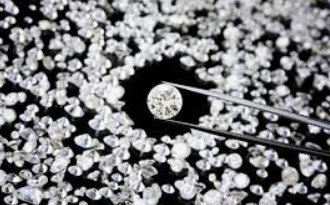 Diamond held with tweezers over a pile of rough diamonds